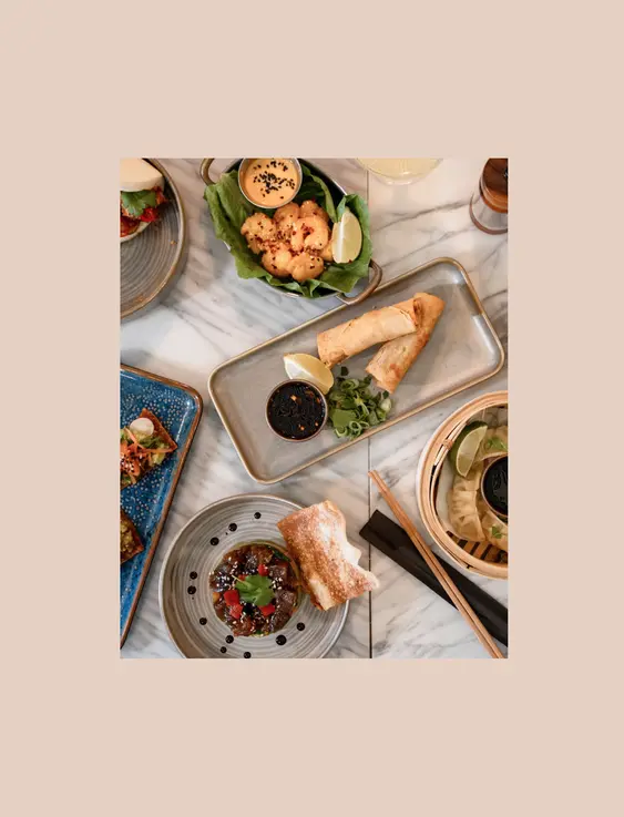 A table full of asian fusion food including; spring rolls, gyoza, prawns, bao buns and more.