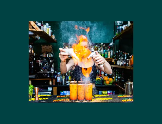 person making 3 passionfruit cocktails with flame on top.