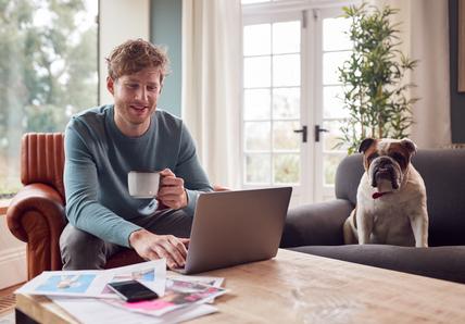 A man sits with a cup of tea next to his Bulldog while working from home