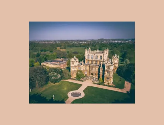 Aerial view of a grand historic mansion set in extensive green parkland.