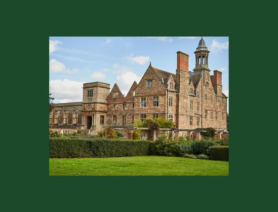 A large, picturesque stone mansion surrounded by lush greenery under a blue sky.