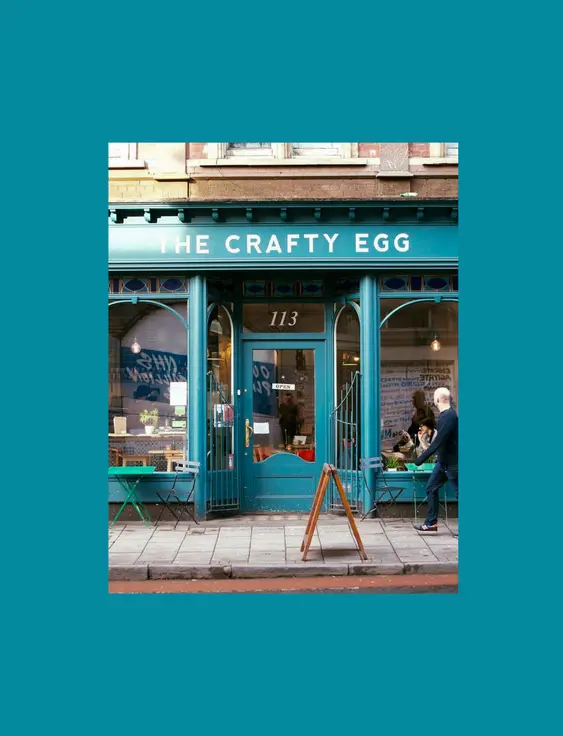 The blue front of the crafty egg cafe with a man walking across the front.