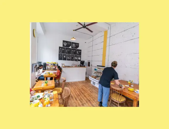 Bright café interior with people dining, wooden furniture, and a minimalist coffee bar.
