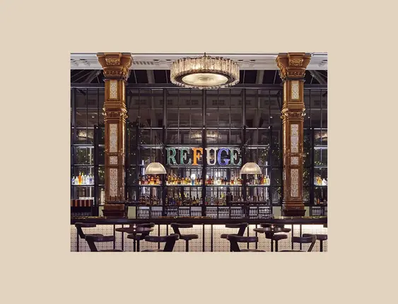 Opulent bar interior with ornate golden columns and intricate tiled pillars, featuring a well-lit bar counter, plush seating, and a 'REFUGE' neon sign in the background.