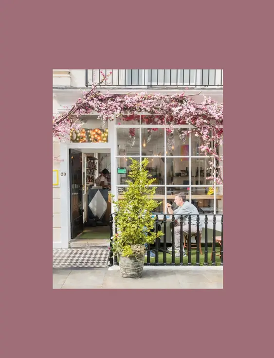 Charming corner café with outdoor seating, adorned with blooming purple wisteria, where patrons enjoy conversation on a city street.