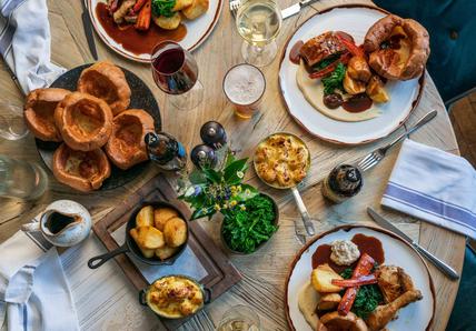 A round wooden table topped with 3 roast dinners, sides of roast potatoes and cottage cheese.