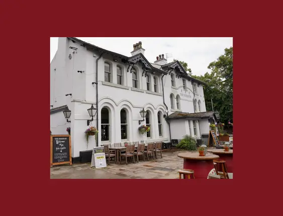 White historic pub building, "The Didsbury," with outdoor seating and arch windows under a cloudy sky.