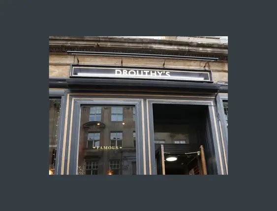 Facade of Drouthy's pub with gold signage, showcasing Scottish ales and spirits, in an elegant building.
