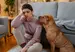 A woman in a pink sweater looks sad sat next to a brown dog
