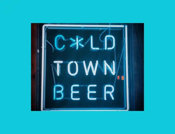 Neon sign reading "Cold Town Beer" mounted on a dark wooden wall, glowing in blue and white.