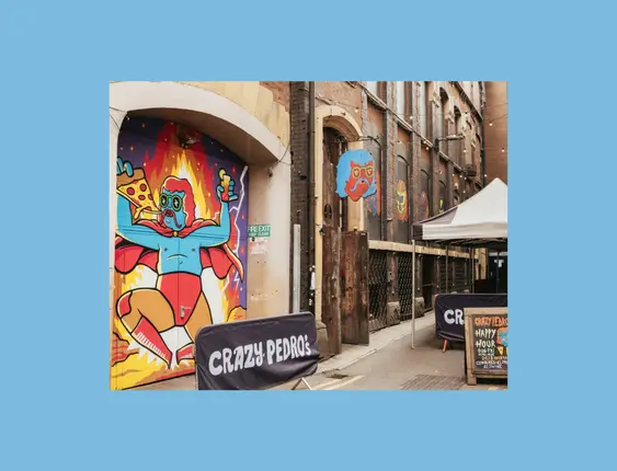 Alleyway entrance to "Crazy Pedro's" featuring vibrant, comic-style mural of a character holding pizza