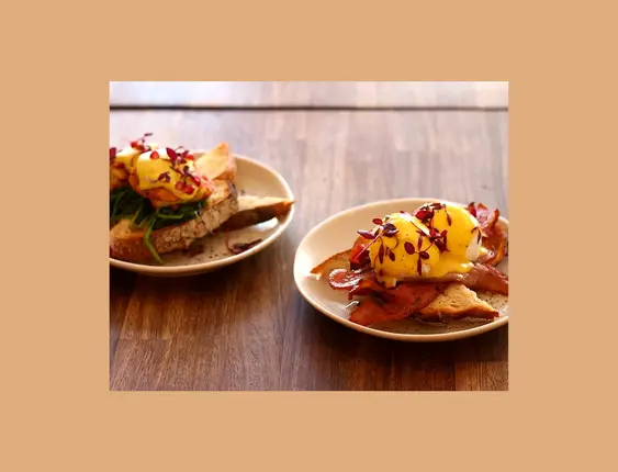 Eggs benedict on toast garnished with red leaves.