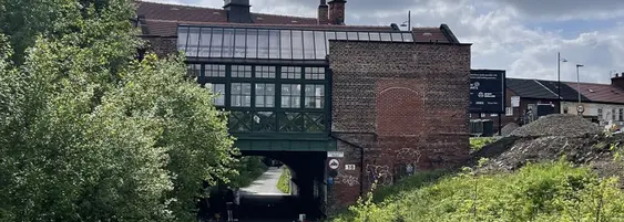 A panoramic view of a unique building featuring a Tudor-style upper section with many windows, sitting atop a brick structure over a pathway.