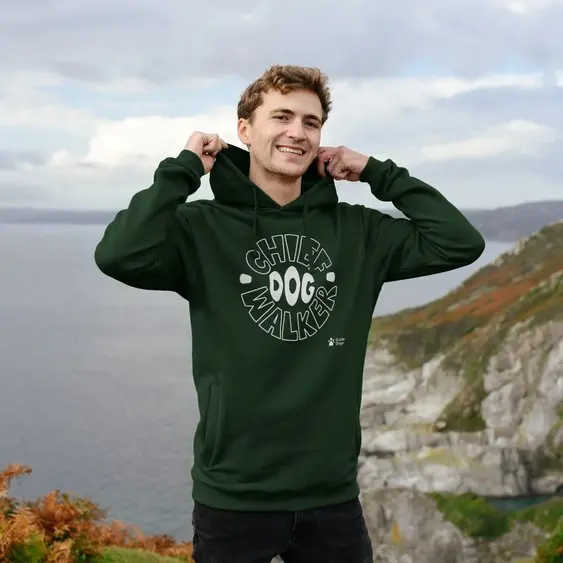 A man wears a green hoodie while smiling and standing outside, the hoodie reads "Chief Dog Walker"