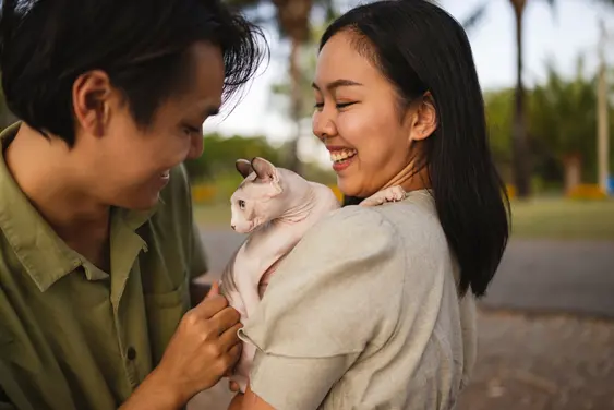 A couple on a date smile as one of them holds their Sphynx cat, they're having an enjoyable time