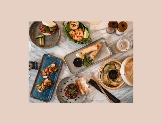 A table full of asian fusion food including; spring rolls, gyoza, prawns, bao buns and more.