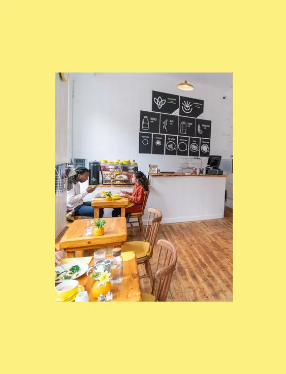 Bright café interior with people dining, wooden furniture, and a minimalist coffee bar.