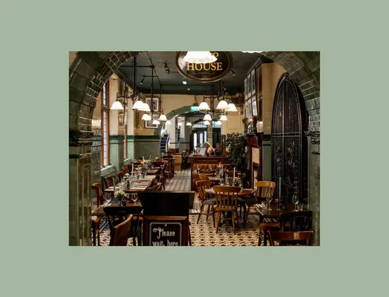 Victorian-style restaurant interior with green tiled walls and archways, featuring a long dining area with wooden tables and hanging lights.