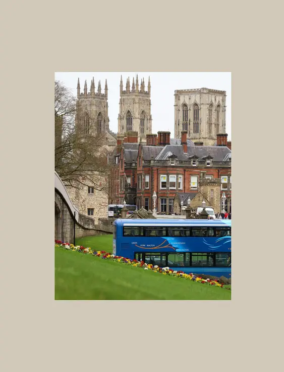 York cathedral standing tall behind buildings, with a blue bus in the foreground.