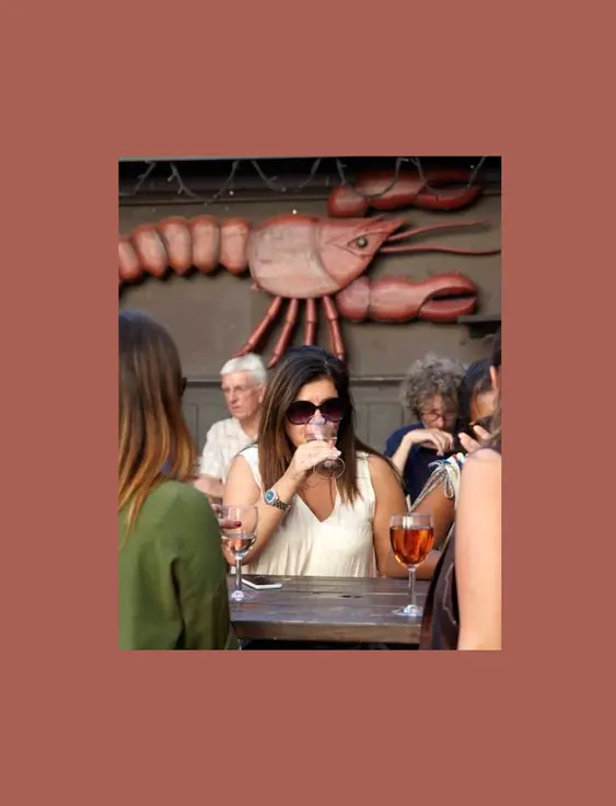 People drinking wine on a pub bench with a lobster on the wall in the background.