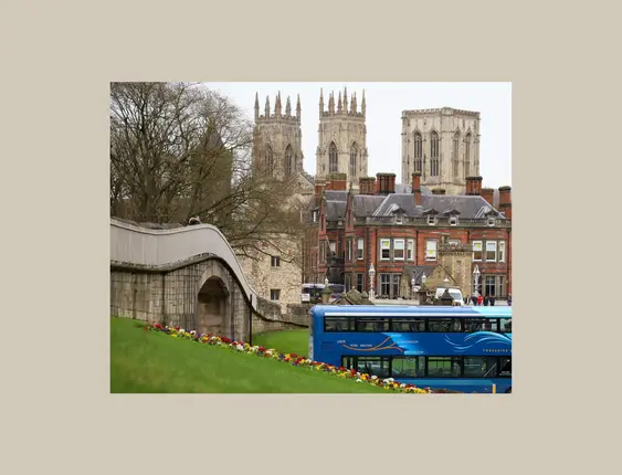 York cathedral standing tall behind buildings, with a blue bus in the foreground.