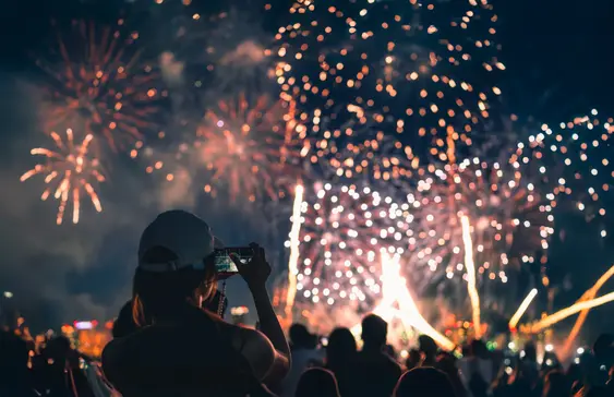 A woman takes a photo of a firework display outdoors