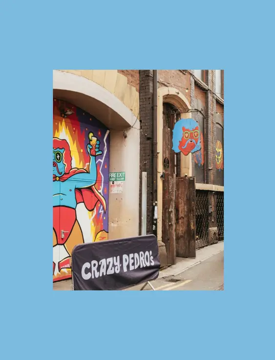Alleyway entrance to "Crazy Pedro's" featuring vibrant, comic-style mural of a character holding pizza.